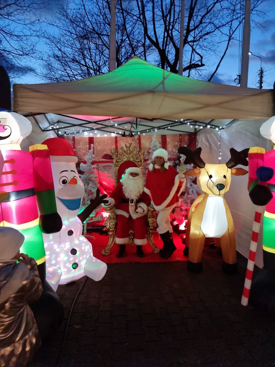 Świąteczna strefa animacji: Mikołaj siedzi na tronie, obok pomocnica Mikołaja, dmuchany bałwan i renifer. W tle namiot oświetlony lampkami.