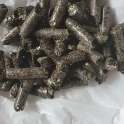 Ciemne, cylindryczne granulki paliwa na pogniecionym, białym papierze, widoczne pęknięcia i struktura materiału.