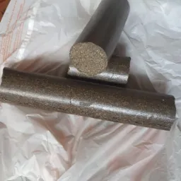 Trzy cylindryczne brykiety na białej, pogniecionej torbie foliowej. Jeden brykiet leży poziomo, drugi oparty na nim pionowo, a trzeci w tle, również poziomo.