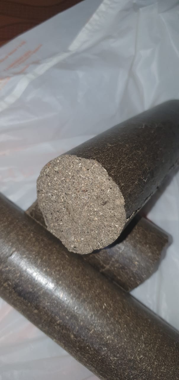 Bliski plan trzech cylindrycznych brykietów z ciemnego, sprasowanego materiału organicznego, z widoczną strukturą włókien, ułożonych na tle z białej folii.