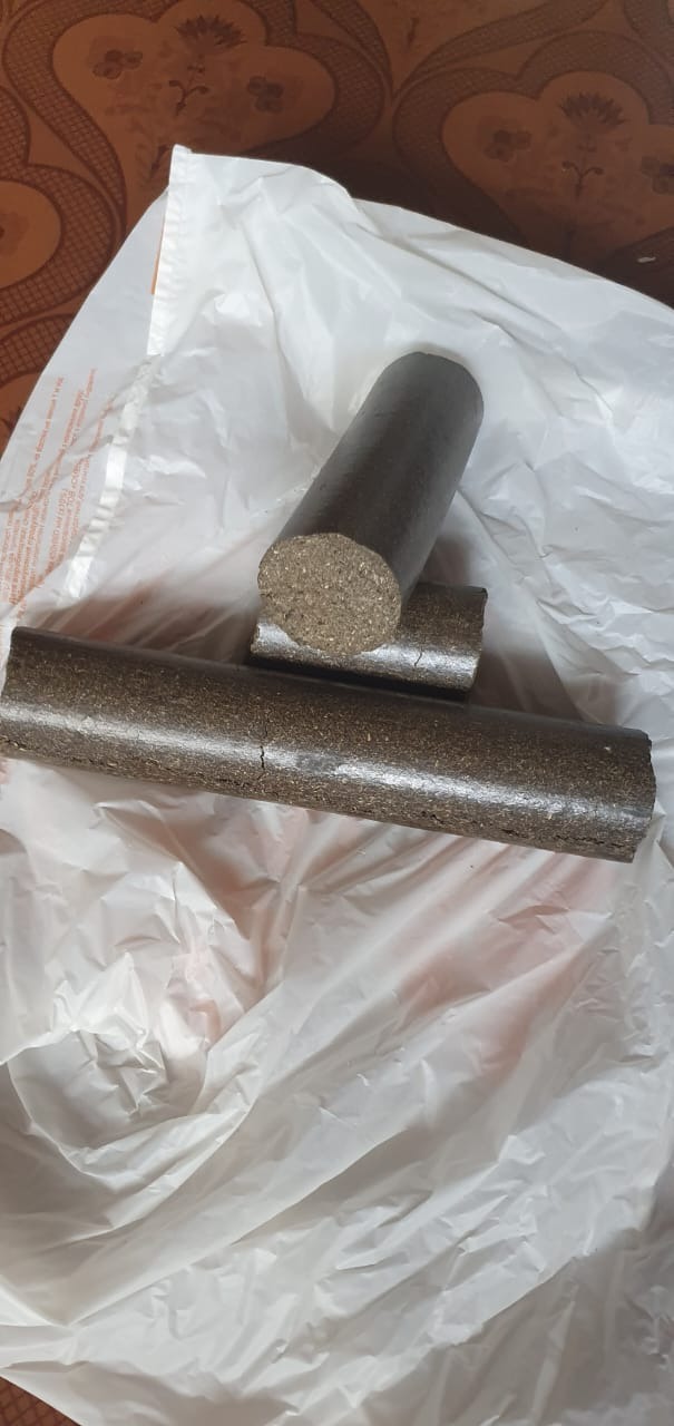 Trzy cylindryczne brykiety na białej, pogniecionej torbie foliowej. Jeden brykiet leży poziomo, drugi oparty na nim pionowo, a trzeci w tle, również poziomo.