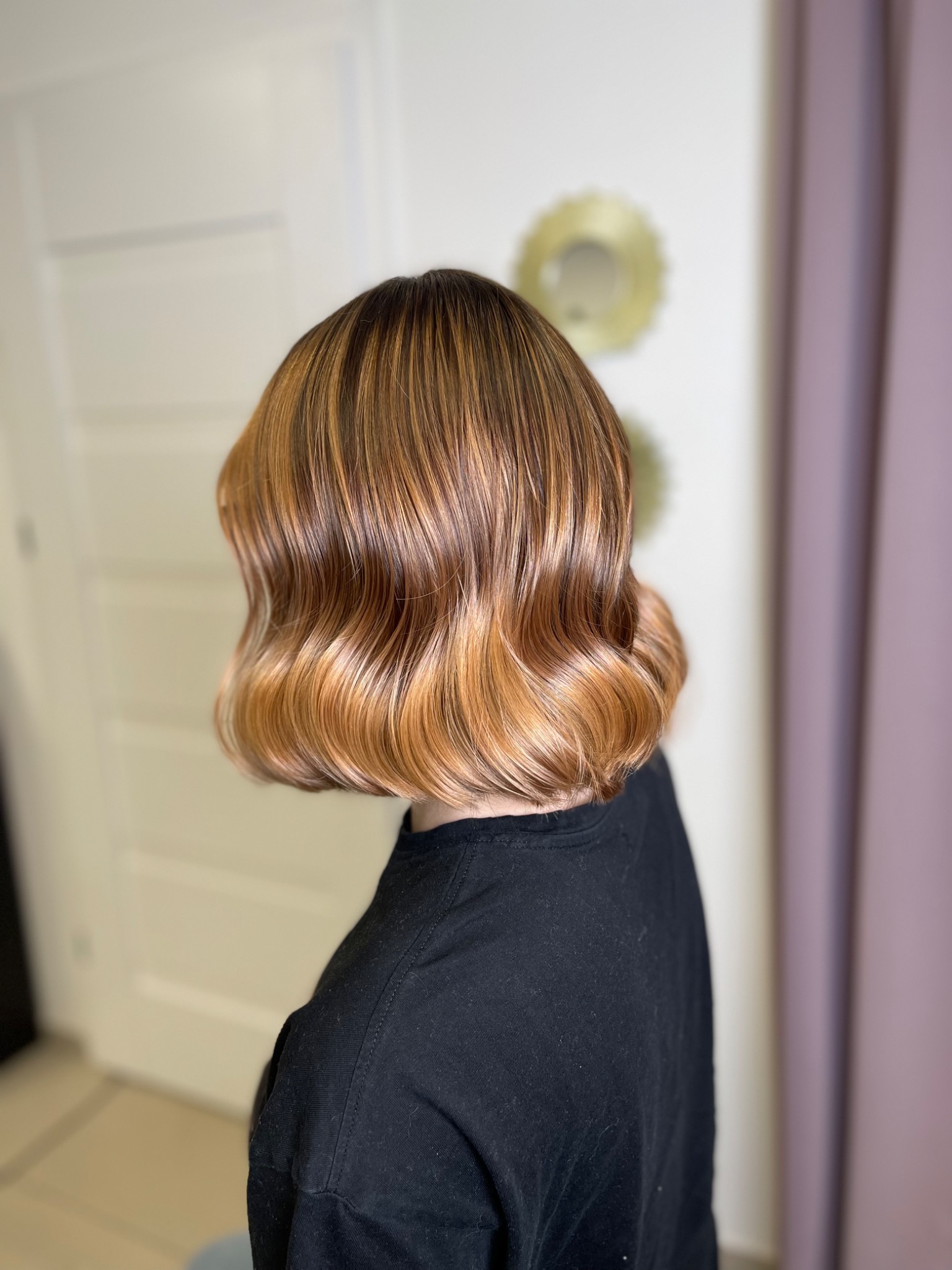 Krótkie, falowane włosy w odcieniach blondu i brązu, widoczne od tyłu, z delikatnym połyskiem i precyzyjnym ułożeniem.