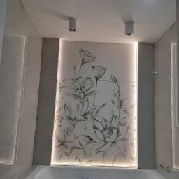 Nowoczesna łazienka z wanną, wyłożona płytkami imitującymi marmur, z dekoracyjnym panelem z motywem kwiatowym podświetlonym LED, oraz punktowymi lampami sufitowymi.