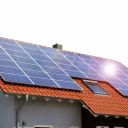 Dom z szarą elewacją i pomarańczową dachówką, na której zamontowano niebieskie panele słoneczne; widoczny komin, okno dachowe i rynna.