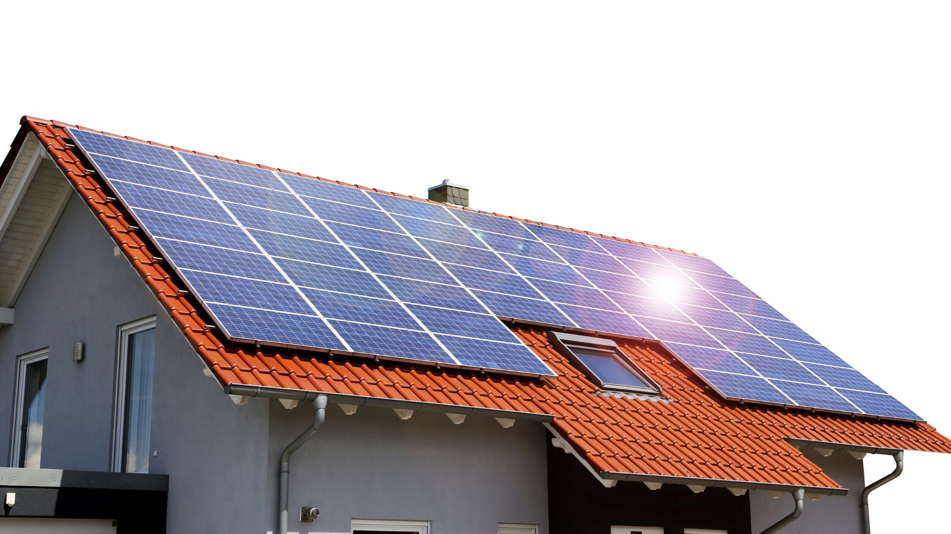 Dom z szarą elewacją i pomarańczową dachówką, na której zamontowano niebieskie panele słoneczne; widoczny komin, okno dachowe i rynna.