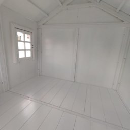 AGO Adam Grabowski - Wnętrze małego, białego domku z drewnianą podłogą i oknem. Widok z dołu, ukazujący konstrukcję dachu i panele ścienne. Minimalistyczny design i jasne oświetlenie.