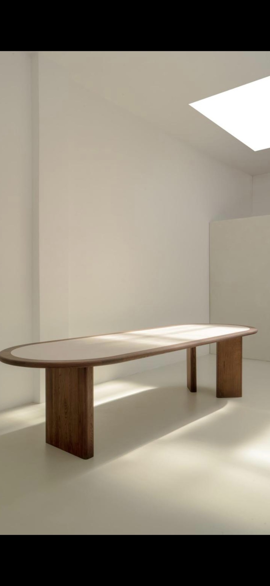 Minimalistyczny stół owalny z drewnianymi nogami w jasnym, nowoczesnym wnętrzu. Naturalne światło podkreśla gładką powierzchnię blatu i prostotę formy.