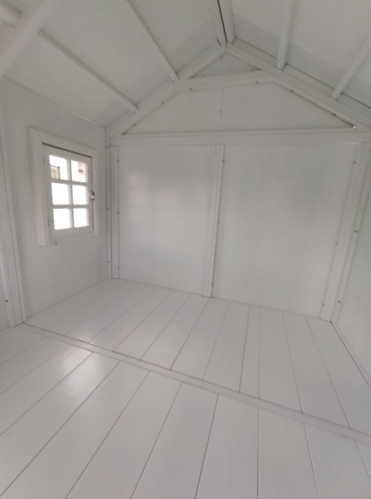 Wnętrze małego, białego domku z drewnianą podłogą i oknem. Widok z dołu, ukazujący konstrukcję dachu i panele ścienne. Minimalistyczny design i jasne oświetlenie.