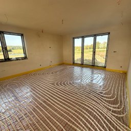 HYDROPIK Paweł Nowak - Układanie rur grzewczych na folii izolacyjnej w jasnym pomieszczeniu z oknami, przygotowanie do wylewki pod ogrzewanie podłogowe.