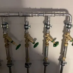 Rozdzielacz hydrauliczny z czterema zaworami z zielonymi pokrętłami, zamocowany na ścianie, instalacja wykonana z metalowych rur.