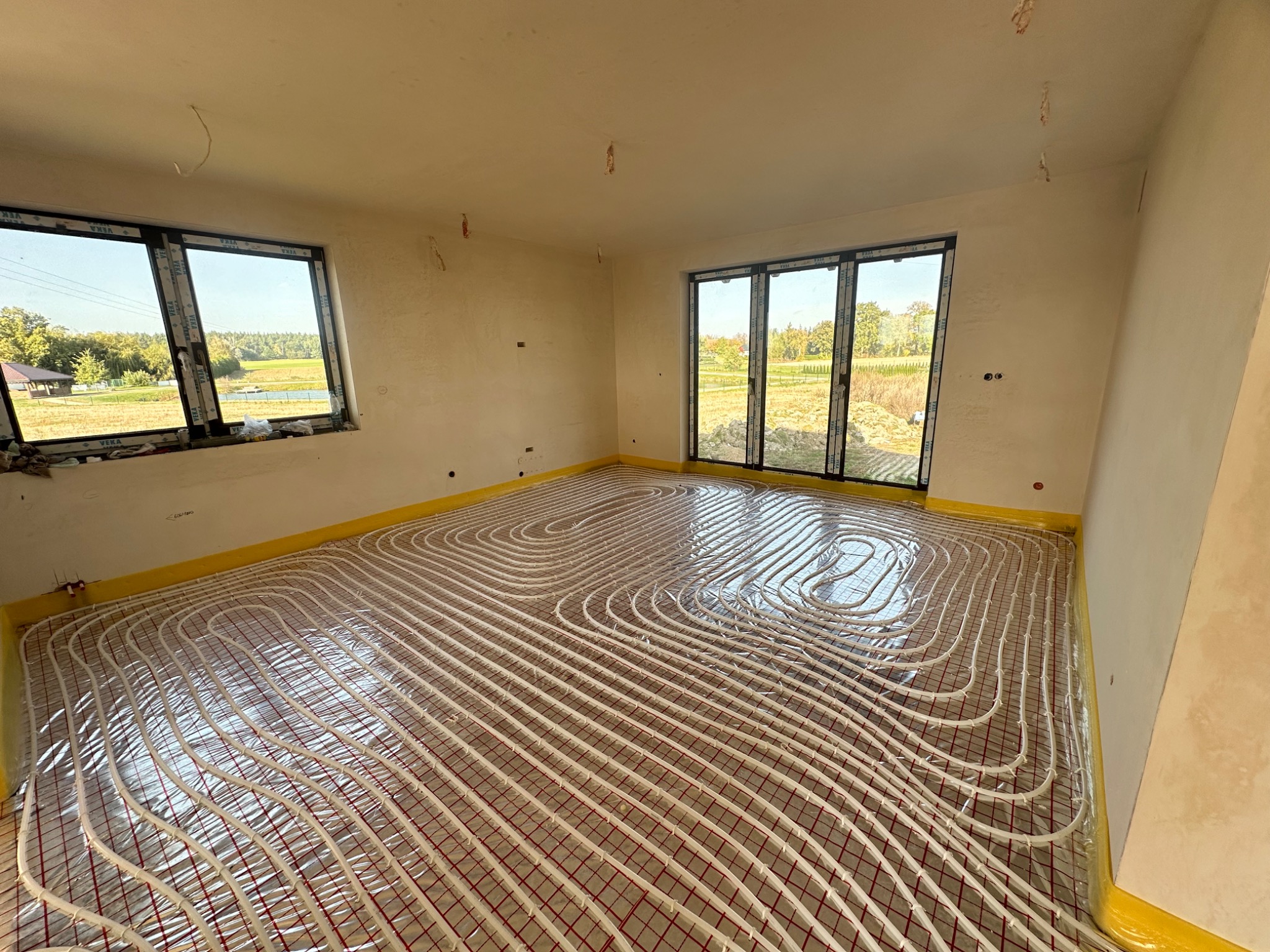 Układanie rur grzewczych na folii izolacyjnej w jasnym pomieszczeniu z oknami, przygotowanie do wylewki pod ogrzewanie podłogowe.