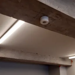 Betonowy sufit z zamontowanym czujnikiem dymu i liniowym oświetleniem LED.