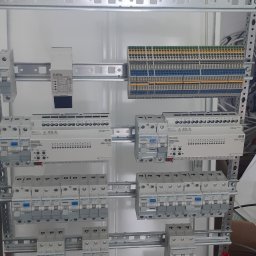 Łukasz Wojtunik Automatyka budynkowa - Rozdzielnia elektryczna z zamontowanymi zabezpieczeniami i modułami, widoczne przewody, listwy zaciskowe i aparatura ABB oraz GIRA.