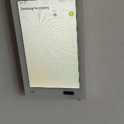 Panel dotykowy Gira G1 na szarej ścianie, wyświetlający menu 'Building functions' z ikonami ustawień i zarządzania budynkiem.