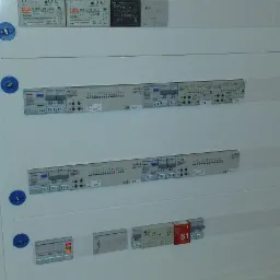 Rozdzielnica elektryczna z zamontowanymi modułami zabezpieczeń, zasilaczami i elementami sterującymi, widoczne oznaczenia i numery obwodów.