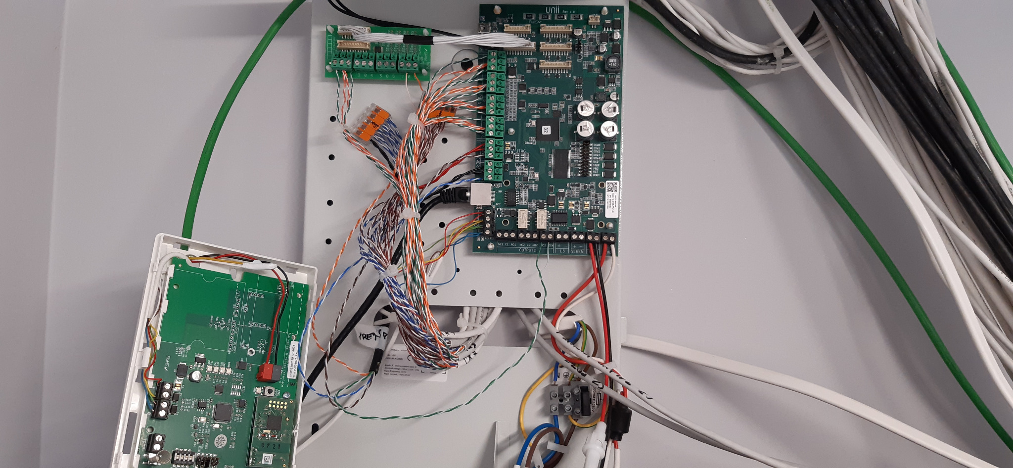 Centrala alarmowa z podłączonymi przewodami i modułami, widoczne złącza, płytki drukowane oraz kable w różnych kolorach.