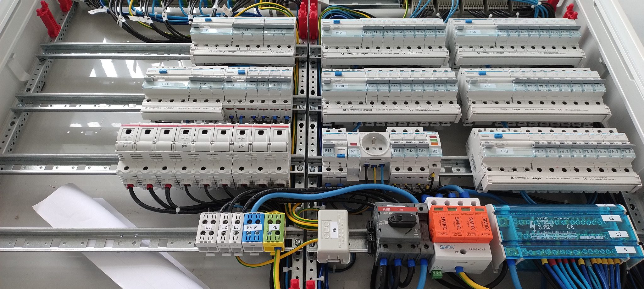 Rozdzielnica elektryczna z zainstalowanymi bezpiecznikami, zabezpieczeniami przeciwprzepięciowymi i listwami zaciskowymi, widoczne kable w różnych kolorach, zamontowana w metalowej obudowie.