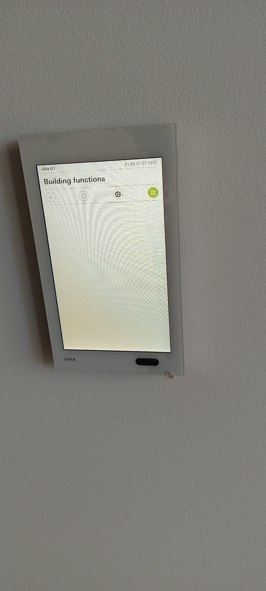 Panel dotykowy Gira G1 na szarej ścianie, wyświetlający menu 'Building functions' z ikonami ustawień i zarządzania budynkiem.