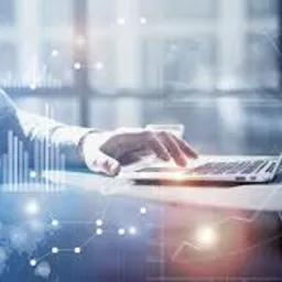 Mężczyzna w jasnej koszuli pracuje na laptopie, na ekranie i w tle widoczne nakładające się wykresy i diagramy, symbolizujące analizę danych i strategie biznesowe.