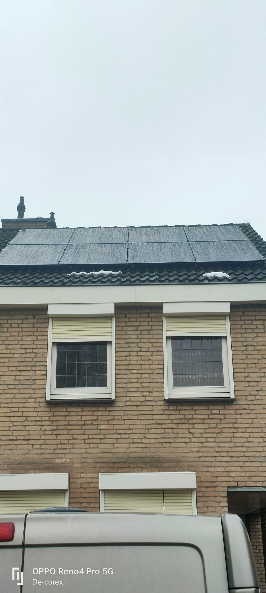 Instalacja paneli słonecznych na dachu domu w Venray, widoczne panele pokryte wodą lub śniegiem, ceglana elewacja budynku z oknami z roletami.