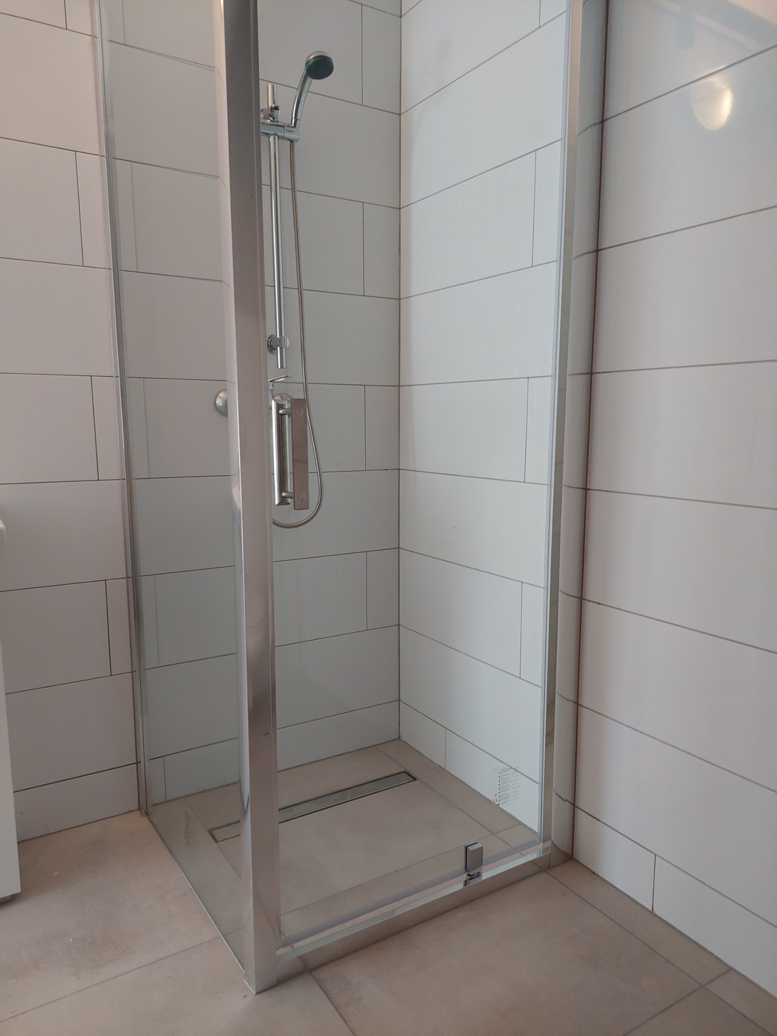 Nowoczesna kabina prysznicowa z chromowanymi profilami i deszczownicą, wyłożona białymi, prostokątnymi płytkami ceramicznymi z delikatną fugą.