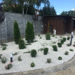 Sławomir Kilichowski - Ogród z białym żwirem, niskimi krzewami i lampami ogrodowymi, obok szopa na narzędzia i zaparkowany samochód.