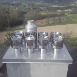 Komplet nowych, błyszczących, nierdzewnych nasad kominowych na szczycie komina, z widokiem na wiejski krajobraz w tle.