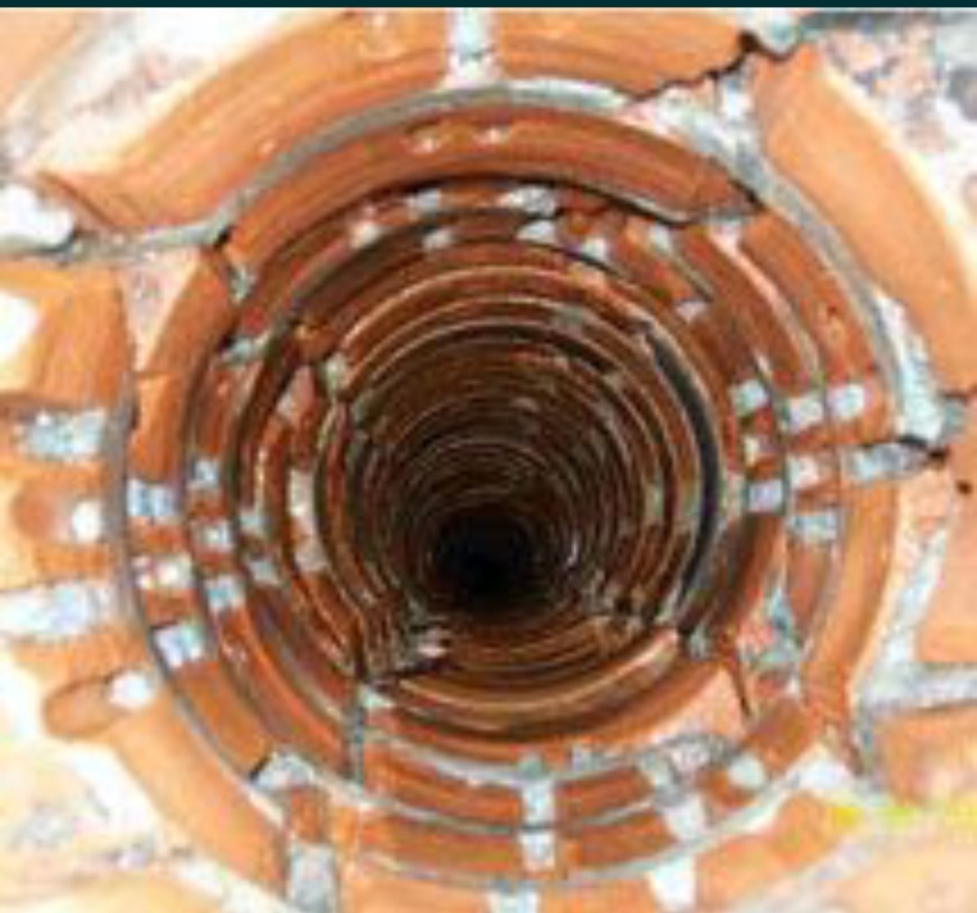 Wnętrze przewodu kominowego wyłożonego cegłą, widok z góry w dół, z widocznymi spękaniami i ubytkami w spoinach.