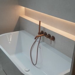 Firma uslugowa Robson - Nowoczesna, biała wanna wolnostojąca z miedzianą armaturą na tle szarej ściany z podświetleniem LED. Minimalistyczny design łazienki na poddaszu.