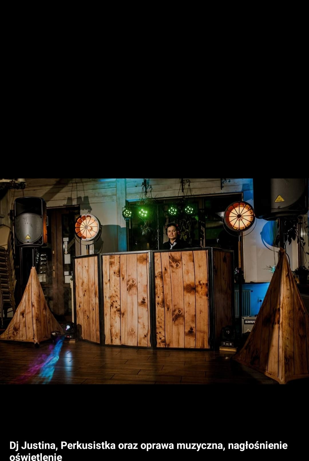 DJ za drewnianym panelem, reflektory z ciepłym światłem, dekoracje w kształcie piramid z drewna, zielone światła w tle, nagłośnienie po bokach.