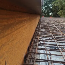 Widok z bliska na siatkę zbrojeniową ułożoną na szalunku, przygotowaną do zalania betonem. Widoczne detale łączeń drut&oacute;w i struktura szalunku.