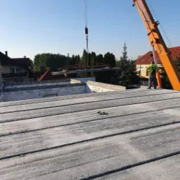 Montaż konstrukcji stalowej dźwigiem na budowie domu z bloczków, widok z góry na strop z płyt prefabrykowanych.