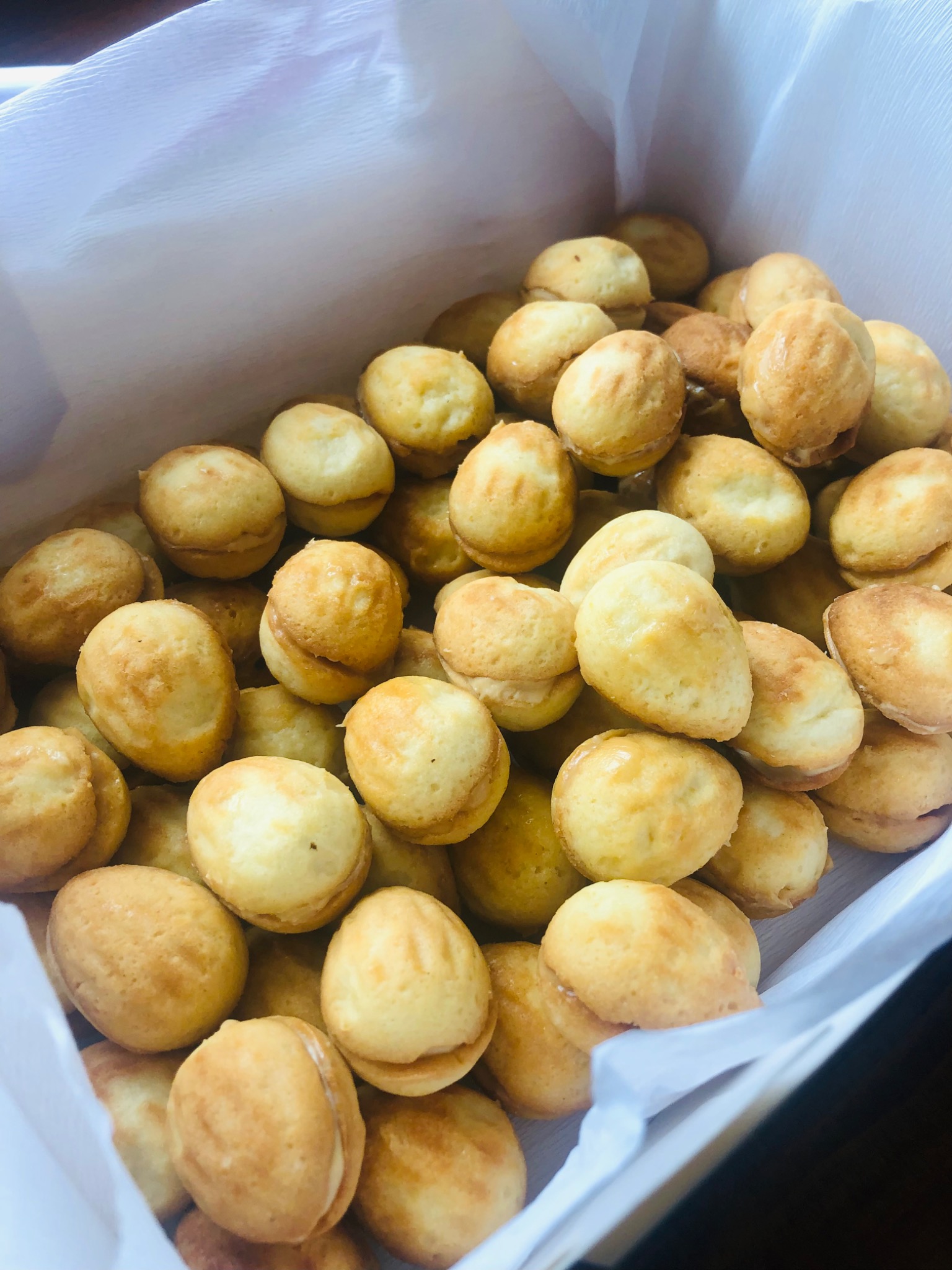 Kartonowe pudełko wypełnione orzechami z kremem, ciasteczka o jasnobrązowej barwie, widoczne delikatne pęknięcia na powierzchni niektórych z nich.