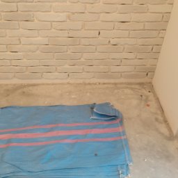 PAWEL - Świeżo pomalowana biała ściana z cegieł, zabezpieczona folią okienna i podłoga przykryta plandeką w niebiesko-różowe pasy