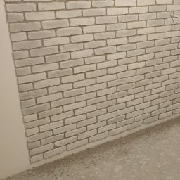 PAWEL - Ściana wykończona dekoracyjną cegłą w odcieniach bieli i szarości, widoczna fuga i surowa podłoga w trakcie remontu.