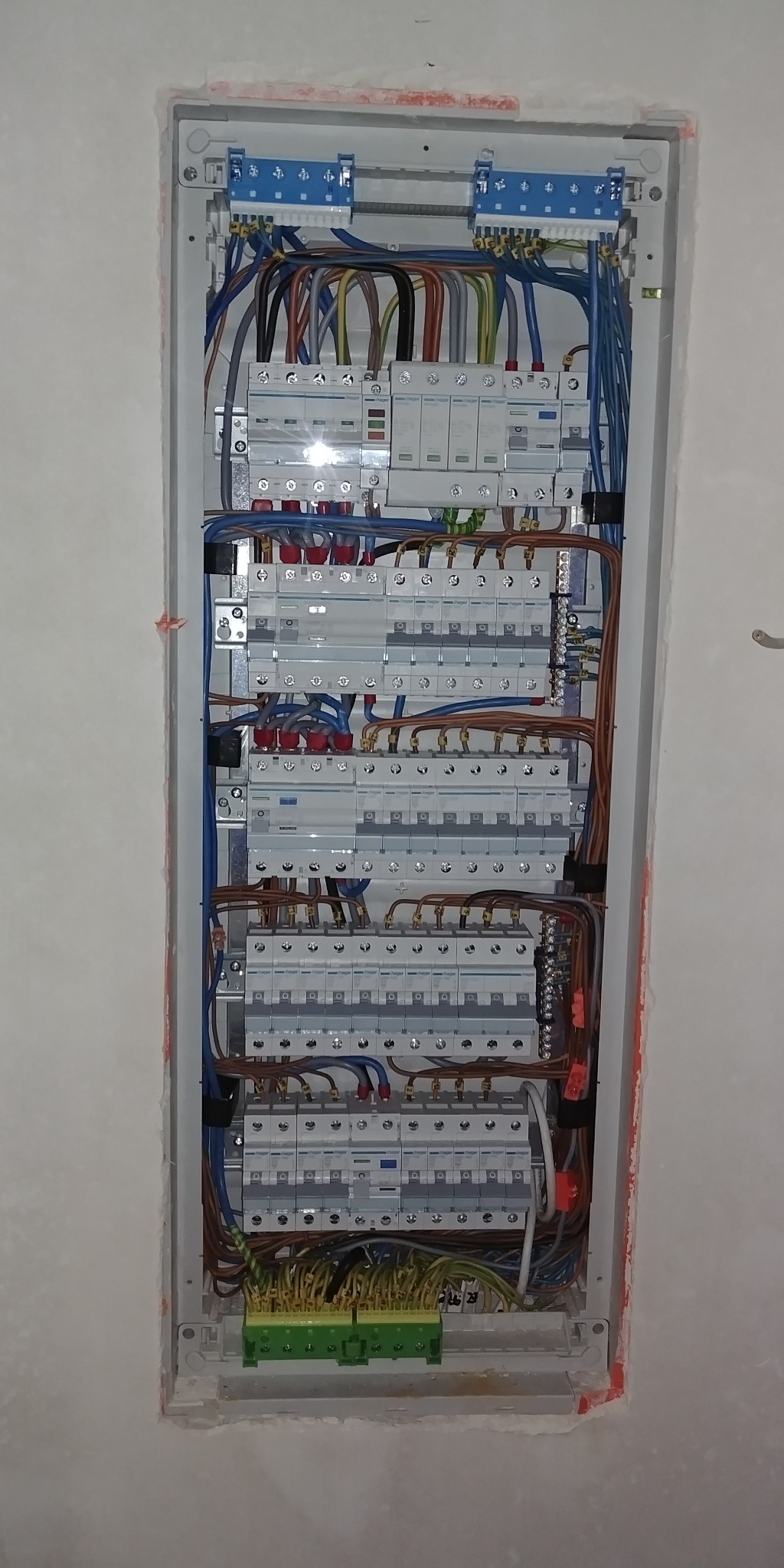 Rozdzielnia elektryczna w trakcie montażu w ścianie, widoczne liczne przewody, bezpieczniki i listwy zaciskowe, ściana wokół rozdzielni nie jest jeszcze wykończona.
