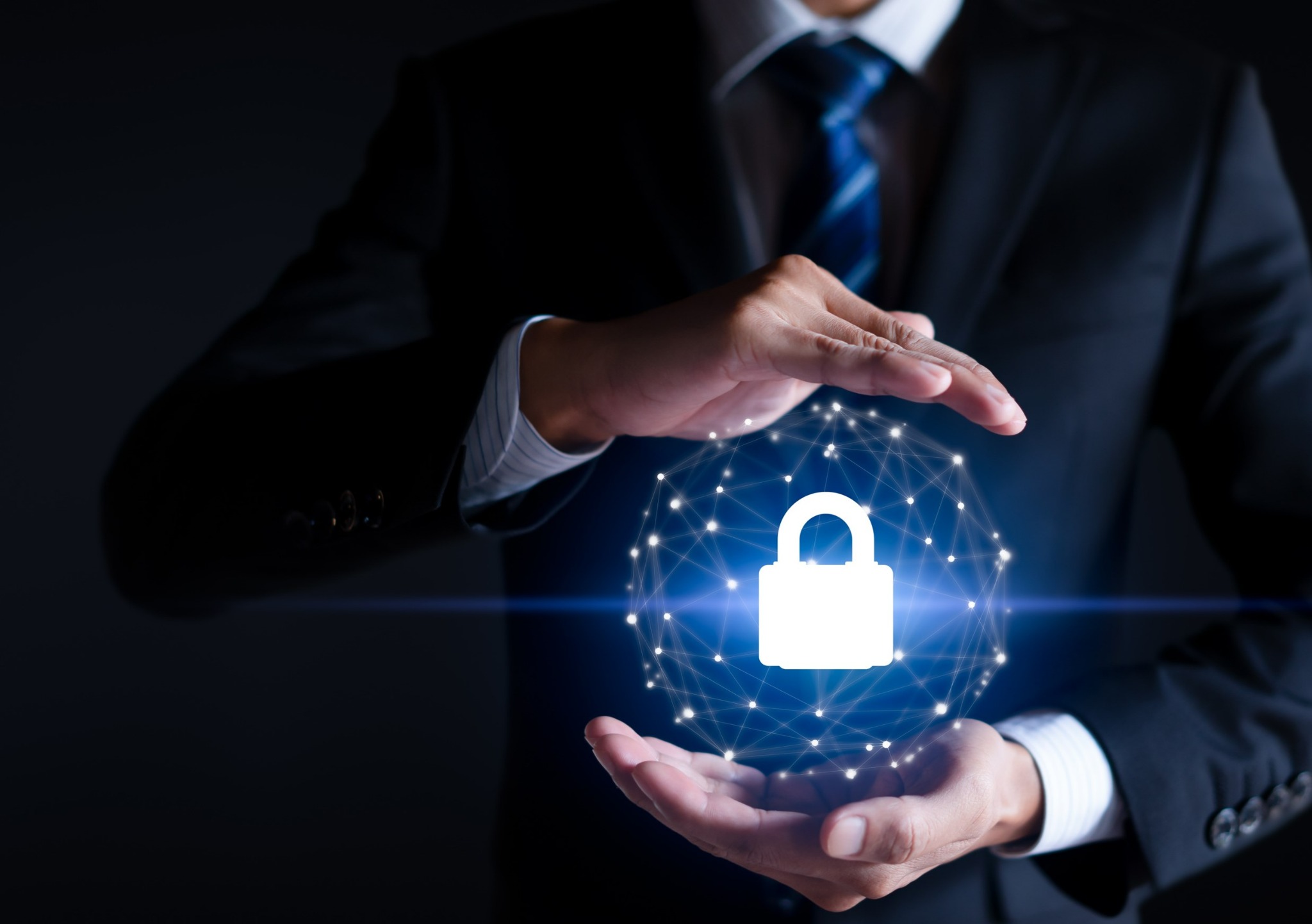 Mężczyzna w garniturze trzyma w dłoniach świecący globus z siecią połączeń i ikoną kłódki, symbolizujący bezpieczeństwo danych.
