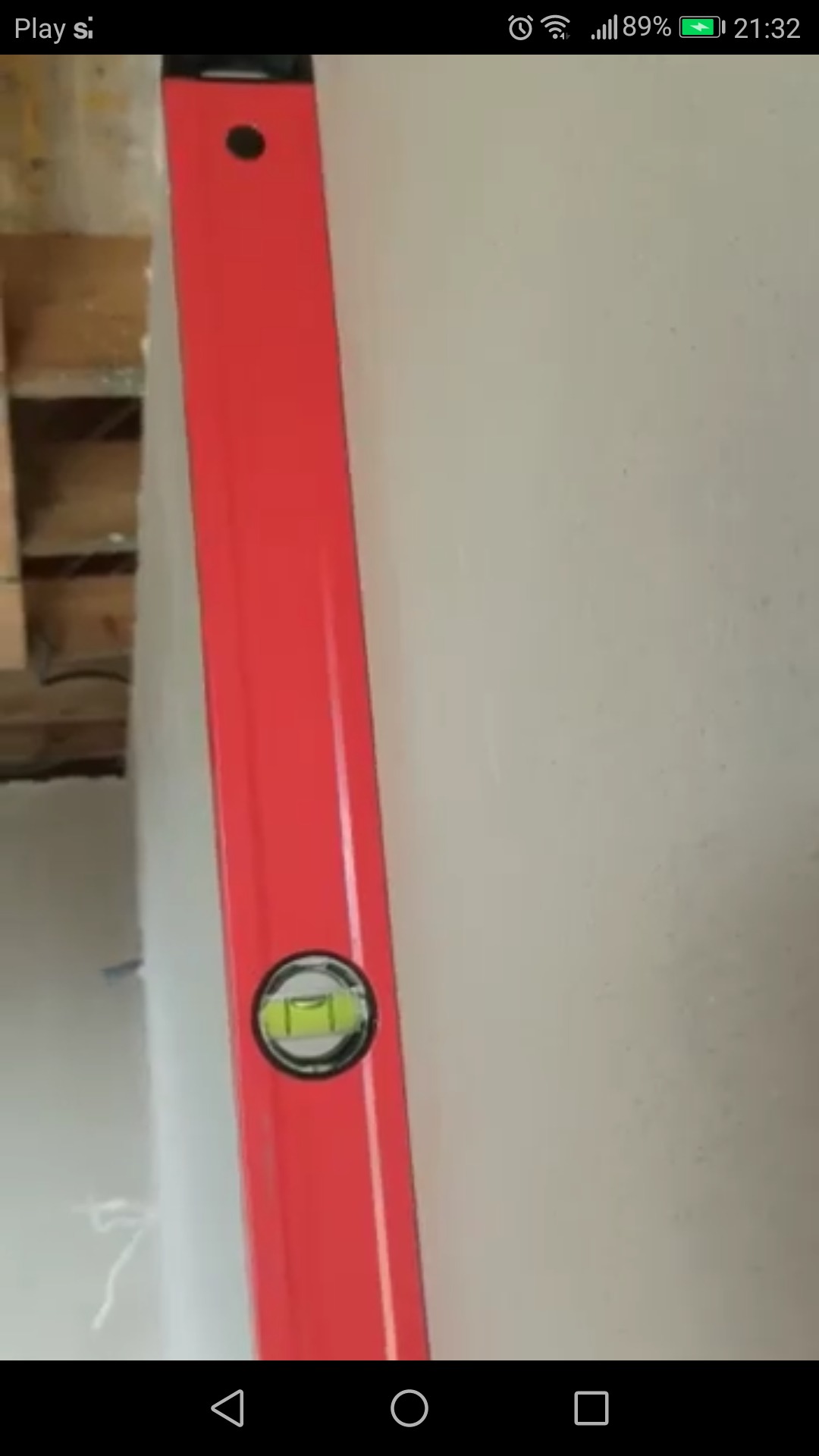 Czerwona poziomica przyłożona do świeżo położonego, jasnego tynku na ścianie w trakcie prac wykończeniowych.