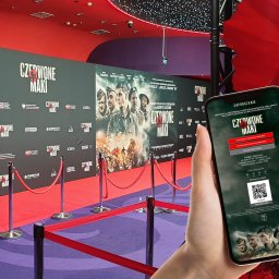 M2 Graphics Mantużyk Marek - Smartfon w dłoni wyświetla zaproszenie na premierę filmu 'Czerwone Maki' na tle plakatu filmowego i czerwonego dywanu.