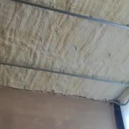 Poddasze ocieplone pianką PUR z widocznymi metalowymi profilami montażowymi i przewodami elektrycznymi, szorstka faktura pianki.