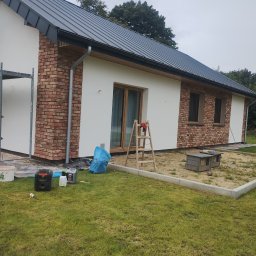 Usługi Remontowo-Budowlane - Dom jednorodzinny z fragmentami elewacji wykończonymi czerwoną cegłą, częściowo otynkowany na biało. Widoczne narzędzia i drabina sugerują trwające prace wykończeniowe.