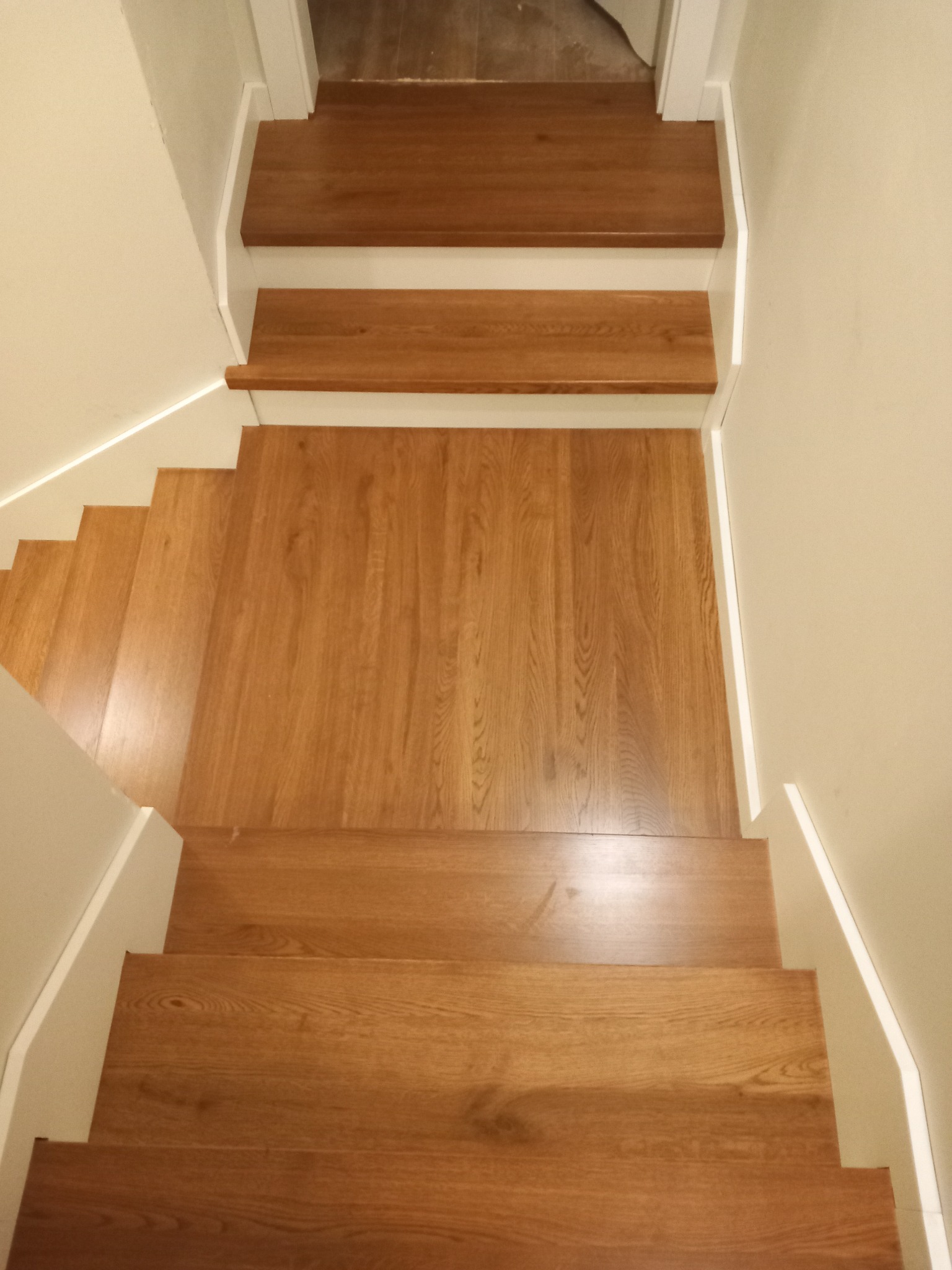 Widok z góry na drewniane schody z dębowymi stopniami i białymi podstopnicami, oświetlone listwą LED przy ścianie.