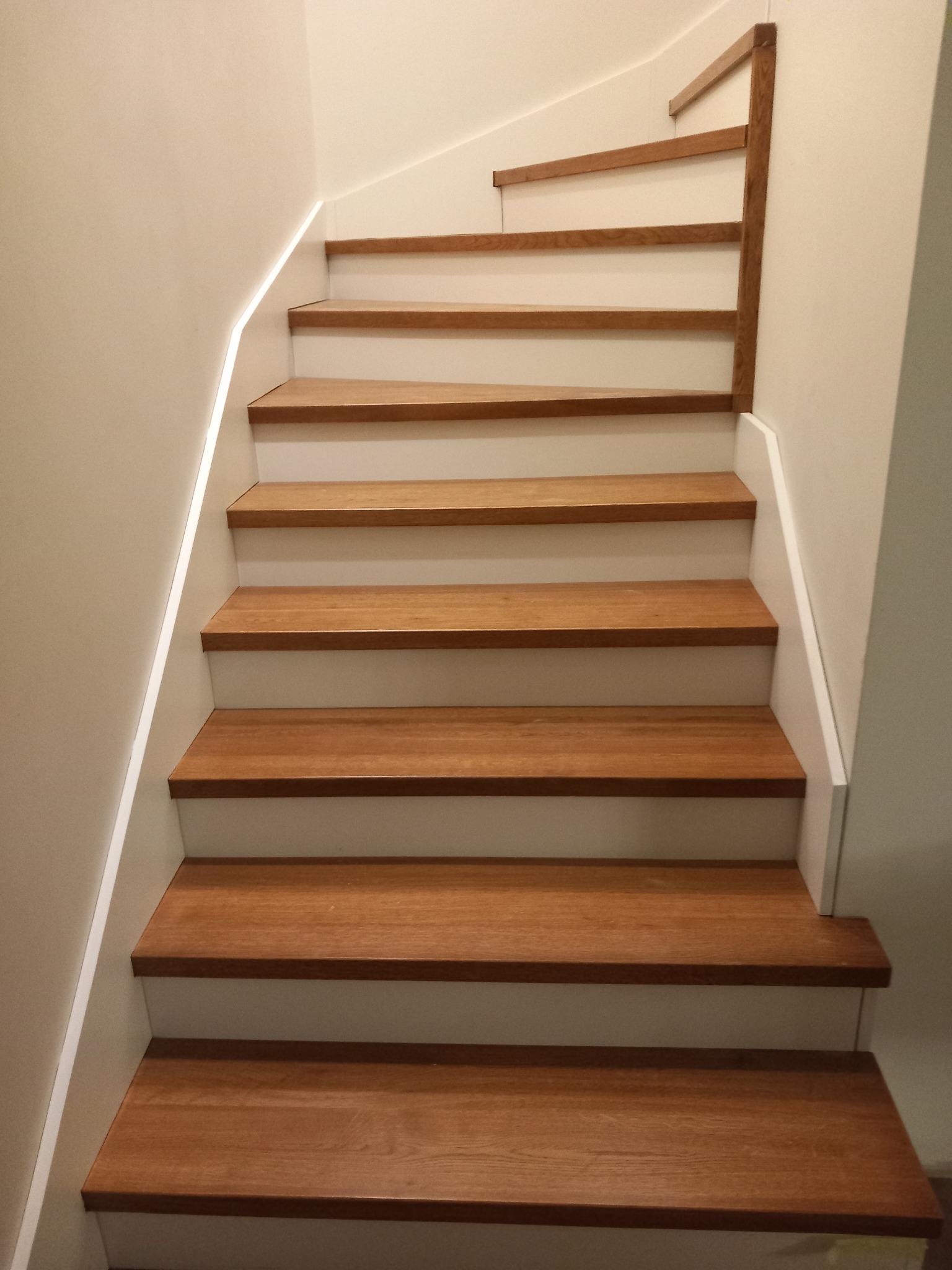 Nowoczesne schody drewniane z białymi podstopnicami, widok z dołu, minimalistyczny design z akcentem na naturalne drewno.