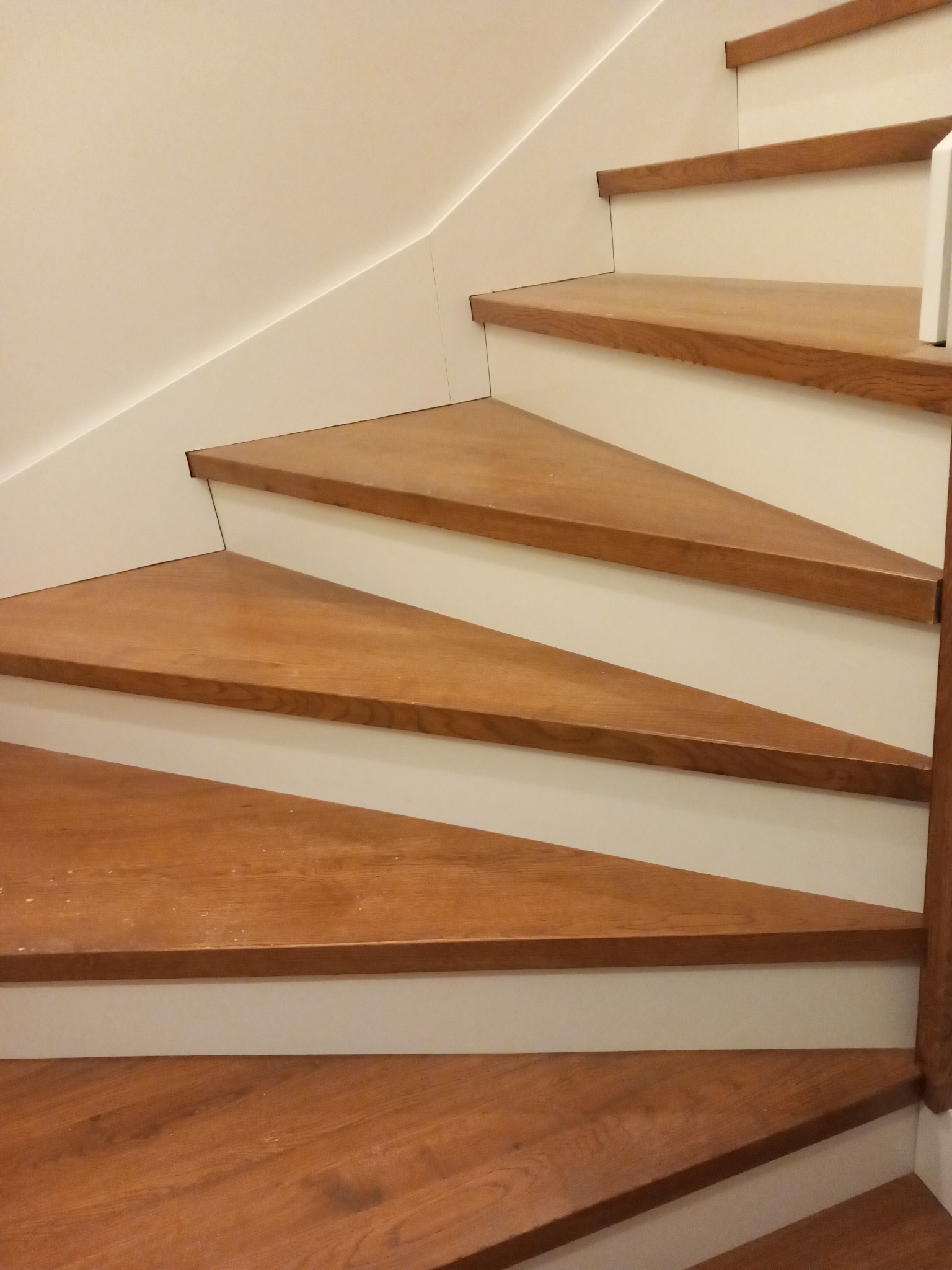 Detale drewnianych schodów z triangularnymi stopniami i białymi podstopnicami, widok z dołu.