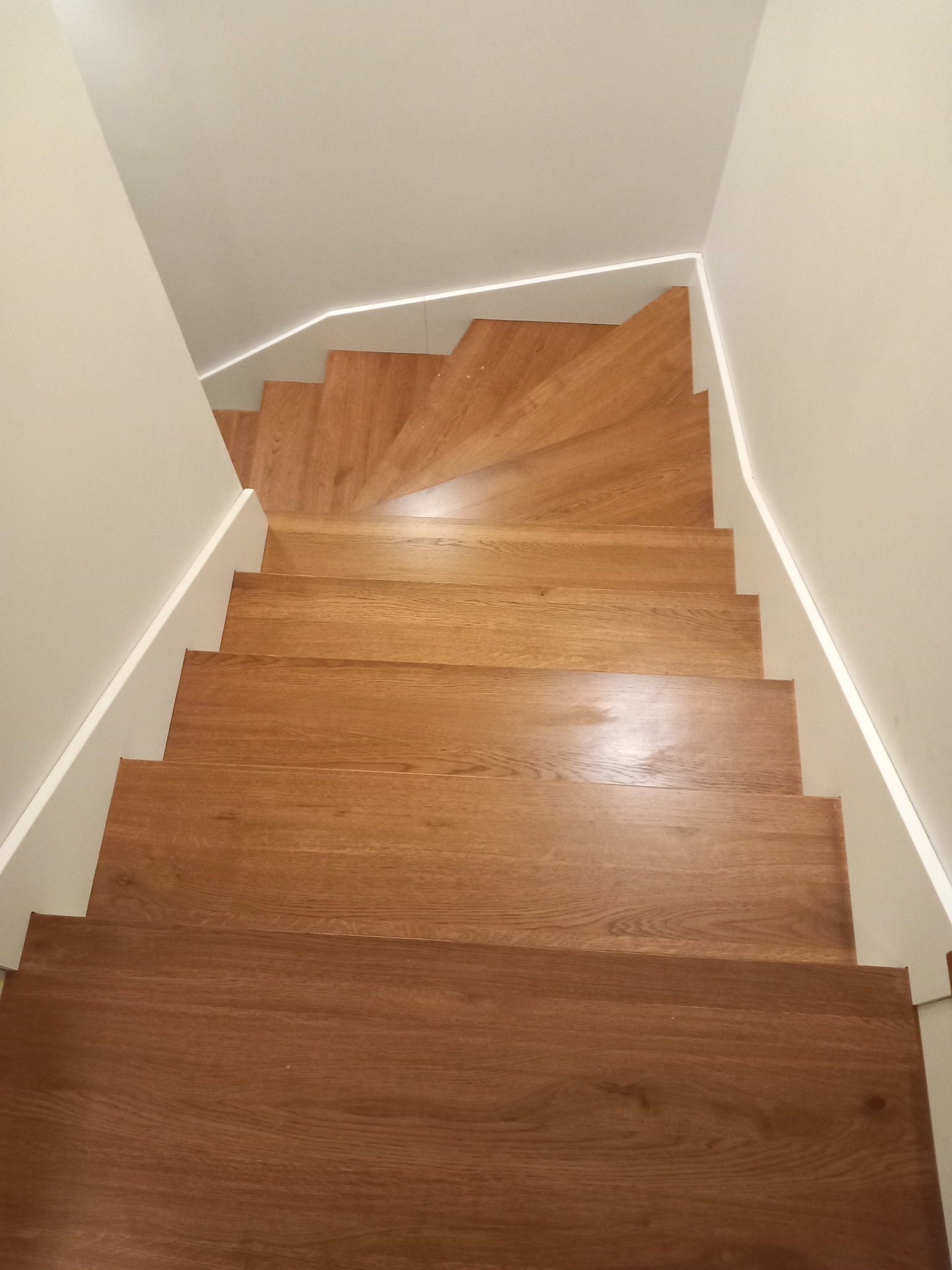 Widok z góry na drewniane schody z oświetleniem LED wzdłuż ściany, tworzące spiralę w nowoczesnym wnętrzu.