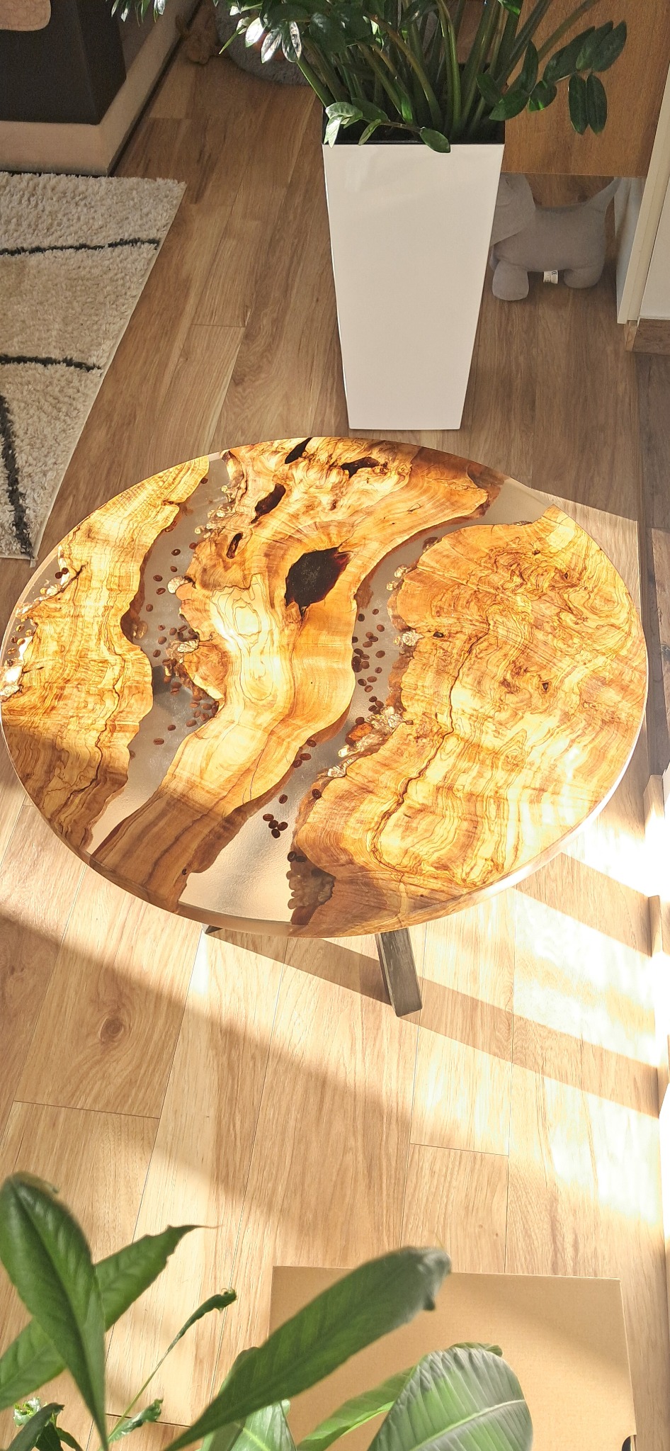 Owalny stolik kawowy z drewna i żywicy epoksydowej, w której zatopione są ziarna kawy. Widok z góry, ciepłe oświetlenie podkreśla unikalny wzór drewna.