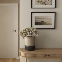 Burzyńska Studio - Beżowe wnętrze: konsola z ryflowanym frontem szuflady, wazon z hortensjami, grafiki w czarnych ramkach na ścianie, minimalistyczne drzwi z czarną klamką.