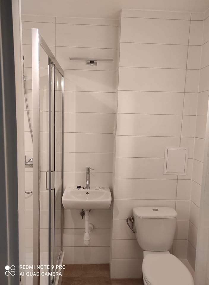 Mała łazienka po remoncie z kabiną prysznicową, umywalką na postumencie i toaletą, wykończona białymi, poziomymi płytkami.