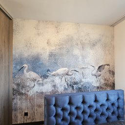 TOM LUX HOME TOMASZ HETNAR - Ściana w sypialni z dekoracyjną tapetą przedstawiającą żurawie, widoczny fragment łóżka z wezgłowiem i szafa przesuwna. Nowoczesny design wnętrza.