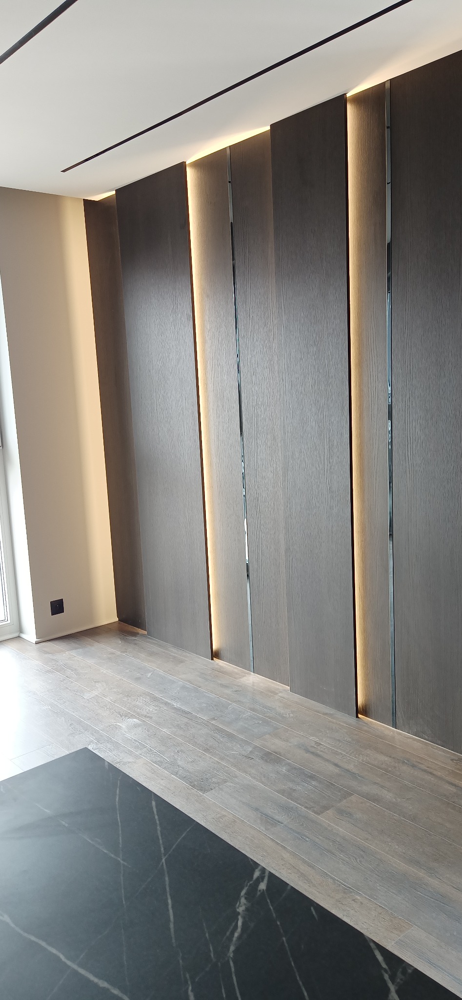 Nowoczesna ściana z paneli drewnianych z wbudowanym oświetleniem LED, widok na podłogę z dwoma rodzajami płytek: imitacja drewna i czarny marmur